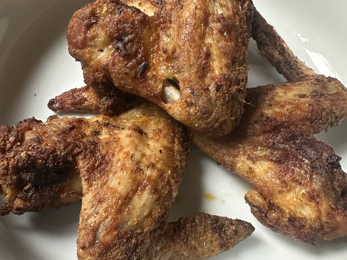 Four golden-brown air fryer chicken wings in a white bowl